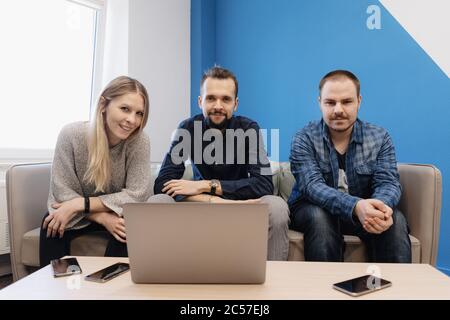Kleiner weicher Besprechungsbereich in der Chill-Out-Zone des Büros mit drei Personen, die beim Arbeitstreffen oder Gespräch am Tisch posieren Stockfoto