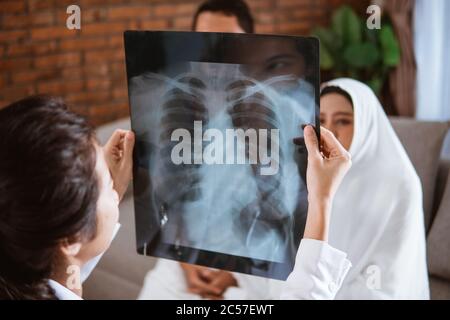 Arzt, der eine muslimische Patientin aus nächster Nähe auf Röntgenstrahlen blickt Stockfoto