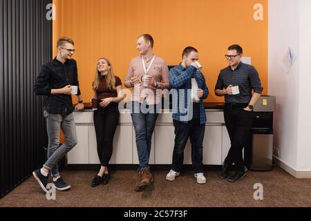 Fröhliche Kollegen haben Spaß an der Mittagspause im Büro, lächelnde multirassische Mitarbeiter lachen und trinken Kaffee. Stockfoto