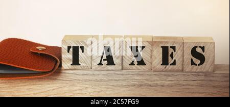 Steuern Wort auf Holzblöcke und Brieftasche auf dem Tisch. Besteuerung und Gebühren Geschäftskonzept Stockfoto