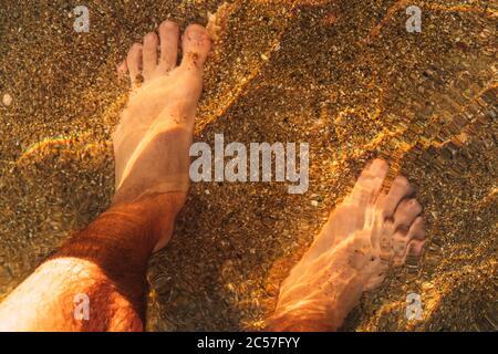 High-Angle-Aufnahme eines Mannes, der am Strand steht Mit den Füßen im Wasser Stockfoto