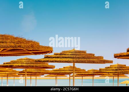 Tropische Strandlandschaft mit Sonnenschirmen. Stroh Sonnenschirme am Strand an einem sonnigen Tag. Sommerzeit, Urlaubskonzept Stockfoto