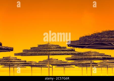 Tropische Strandlandschaft mit Sonnenschirmen. Strohsonnenschirme am Strand bei Sonnenuntergang. Sommer, Urlaubskonzept Stockfoto