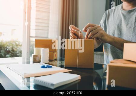 Junge Unternehmer sind binden ein Seil Pappkartons, um die Produkte für Kunden im Home Office zu verpacken. Stockfoto