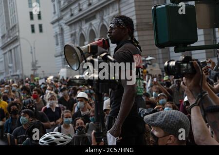 New York, Usa. Juli 2020. Ein Organisationschef der Gruppe Warriors wendet sich bei einem Protest vor dem Rathaus mit einem Megaphon an die Massen.die Spannungen nehmen vor einer Abstimmung des Stadtrates über New Yorks Budget zu, Das ist inklusive des Budgets der Polizeibehörde, da sich Demonstranten, die mit Black Lives Matter (BLM) und anderen Gruppen verbunden sind, in einem Protest vor dem Rathaus in Lower Manhattan versammeln, während sie weiterhin fordern, dass das New York City Police Department (NYPD) definanziert wird. Kredit: SOPA Images Limited/Alamy Live Nachrichten Stockfoto