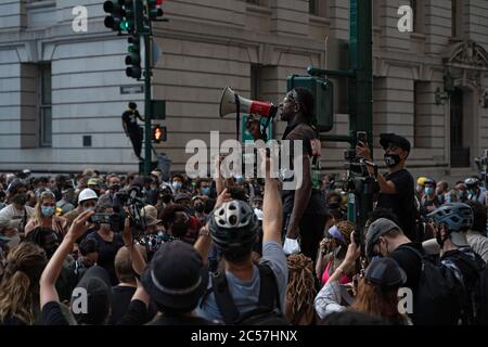 New York, Usa. Juli 2020. Ein Organisationschef der Gruppe Warriors wendet sich bei einem Protest vor dem Rathaus mit einem Megaphon an die Massen.die Spannungen nehmen vor einer Abstimmung des Stadtrates über New Yorks Budget zu, Das ist inklusive des Budgets der Polizeibehörde, da sich Demonstranten, die mit Black Lives Matter (BLM) und anderen Gruppen verbunden sind, in einem Protest vor dem Rathaus in Lower Manhattan versammeln, während sie weiterhin fordern, dass das New York City Police Department (NYPD) definanziert wird. Kredit: SOPA Images Limited/Alamy Live Nachrichten Stockfoto