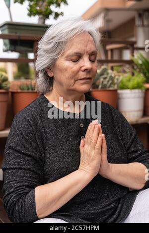 Nahaufnahme einer älteren Frau mit weißem Haar und meditativer Sportkleidung umgeben von Pflanzen Stockfoto