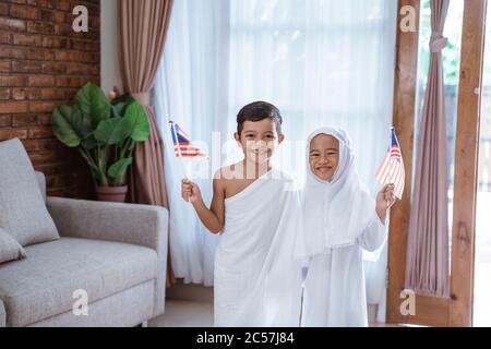 Nettes kleines Kind trägt muslimische ihram Kleidung und Kleid. hadsch und Umrah Konzept mit malaysia Flagge Stockfoto