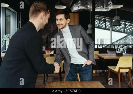 Lächelnde junge Geschäftspartner in Business Casual Wear blicken einander an und schütteln nach Vereinbarung die Hände. Grußkonzept Stockfoto