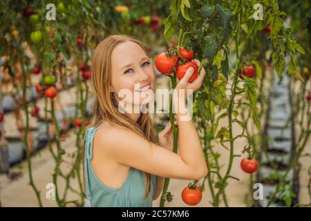 Nahaufnahme einer Frau, die Tomaten auf dem Zweig neben ihrem Gesicht hält, und dabei denkt, sie zu essen Stockfoto
