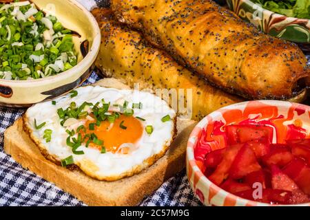 Rustikale Komposition mit Würstchenbrötchen, Spiegelei auf Toast, verschiedenen Schüsseln mit Sauce und gehacktem Gemüse. Stockfoto