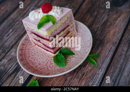 Schmackhaftes Stück Himbeere mehrschichtigen Kuchen auf Teller. himbeerkuchen serviert für Nachtisch auf Holz Hintergrund mit Minzblättern. Köstliche Scheibe Tart auf dem Teller. Himbeerkuchen backen und dekorieren Stockfoto
