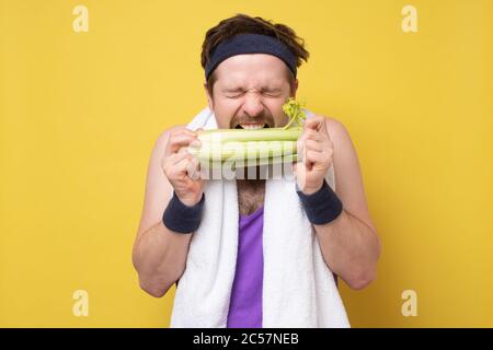 Sportlicher kaukasischer junger Mann, der einen Sellerie beißt Stockfoto