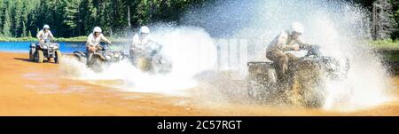 Vier Männer fahren Motocross ATV Quad durch spritzende Fluss See Wasser mit hoher Geschwindigkeit. Foy, Foyross Lake, Sudbury, Kanada. Stockfoto