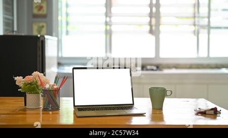 Ein weißer leerer Bildschirm Computer Laptop setzt auf einem hölzernen Schreibtisch in der Küche. Stockfoto