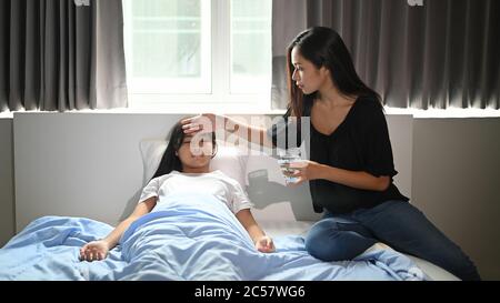 Eine junge Mutter kümmert sich im Schlafzimmer um ihre kranke Tochter. Stockfoto