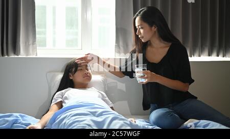 Eine junge Mutter kümmert sich im Schlafzimmer um ihre kranke Tochter. Stockfoto