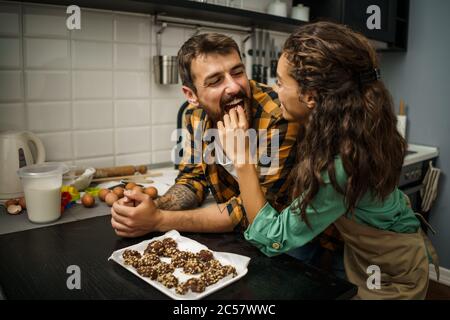 Glückliches multiethnisches Paar haben in ihrer Küche Kekse gemacht. Der Mensch ist bereit, es zu probieren. Stockfoto