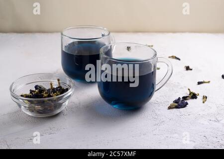 Anchan Thai blauer Tee in zwei Glas-Tassen und einer Schüssel mit trockenen Blumen. Schöne Indigo-Farbe. Speicherplatz kopieren. Stockfoto