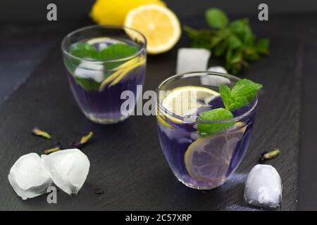 Anchan erfrischender blauer Thai Tee in Gläsern mit Eis und Zitrone auf schwarzem Hintergrund. Stockfoto