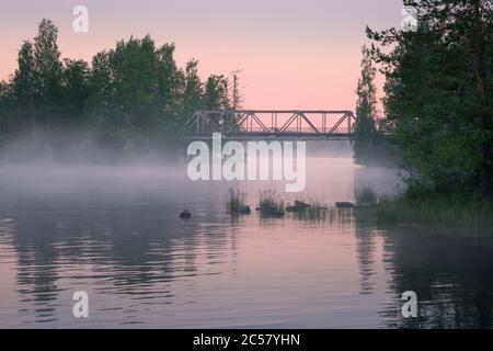 Neblige Sommerlandschaft und alte Eisenbrücke mit schönen ruhigen See in der Sommernacht in Finnland Stockfoto