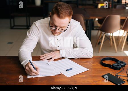 Schöner junger Komponist mit stilvoller Brille schreibt mit Stift musikalische Noten Stockfoto