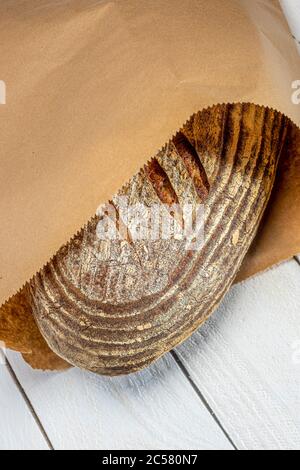 Frisch gebackener Sauerteig Brot in braunem Papierbeutel auf weiß getünchten Brettern Stockfoto