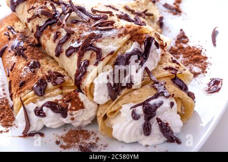 Europäischer Pfannkuchen oder Palatschinke oder Palacinka mit Schlagsahne, verziert mit Schokoladensirup. Stockfoto