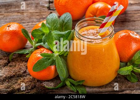 Saft aus frisch gepresster Mandarine und Minze mit reifen Mandarinen, Blättern und altmodischen Trinkhalmen. Stockfoto