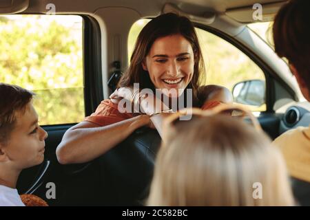 Lächelnde Mutter dreht sich um zu ihren Kindern, die auf dem Rücksitz des Autos sitzen. Glückliche junge Familie auf Reise. Stockfoto