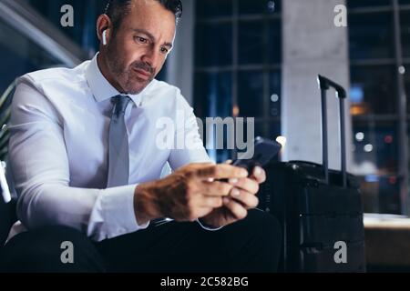 Geschäftsmann, der in der Lounge des Flughafens sitzt und mit seinem Handy eine SMS schreibt. Geschäftsexperte auf einer Geschäftsreise mit dem Handy, während er auf ihn wartet Stockfoto