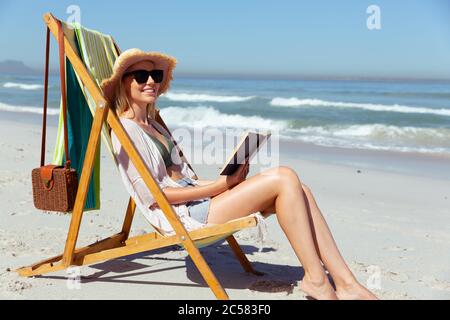 Frau liest ein Buch, während sie am Strand sitzt Stockfoto