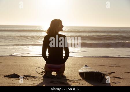 Frau mit Surfbrett am Strand zu sitzen Stockfoto