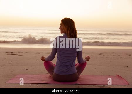 Rückansicht einer Frau, die Yoga am Strand während des Sonnenuntergangs durchführt Stockfoto