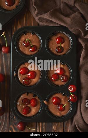 Backen von Schokoladenmuffins. Rohe vegane BananenkirschMuffins mit frischen Beeren auf braunem Holzhintergrund. Draufsicht. Sommeressen Stockfoto