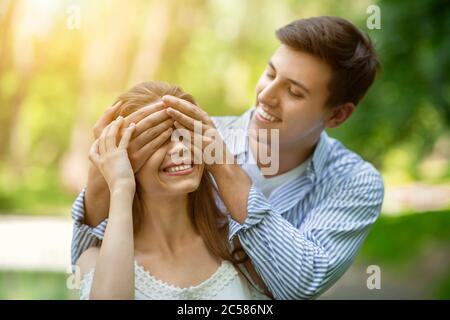 Romantischer Freund schließt die Augen seiner Freundin und spielt Guess Who im Freien Stockfoto