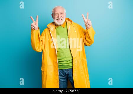 Portrait seiner er nett fröhlich fröhlich zuversichtlich grauhaarigen Mann trägt gelben Kunststoff-Mantel zeigt Doppel V-Zeichen isoliert über hell lebendig Stockfoto