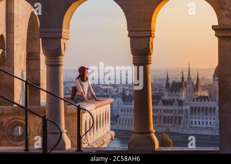 Eine glückliche junge Frau, die ihre Reise zum Schloss von Budapest in Ungarn auf dem Aussichtspunkt von Fischerbastei bei Sonnenaufgang genießt. Stockfoto