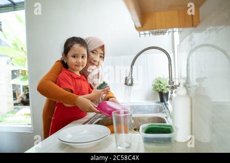 asiatische muslimische Tochter hilft ihrer Mutter in der Küche Geschirr waschen zusammen Stockfoto