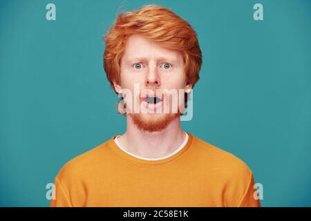 Porträt von geschockt jungen Rotschopf Kerl mit Bart halten Mund offen in Erstaunen vor blauem Hintergrund Stockfoto
