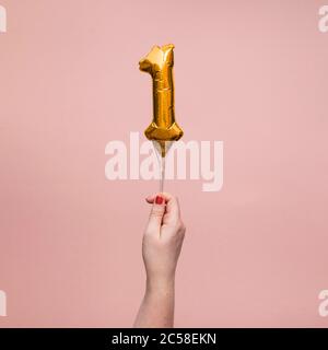 Weibliche Hand hält eine Zahl 1 Geburtstag Feier Gold Ballon Stockfoto