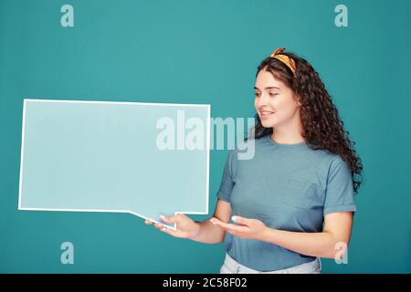 Selbstbewusste junge Frau im Haar Schal zeigt auf Banner in Form von Dialog Wolke, während Informationen vor blauem Hintergrund zu erklären Stockfoto