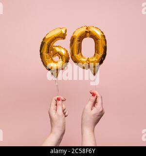 Weibliche Hand hält eine Zahl 60 Geburtstag Feier Gold Ballon Stockfoto