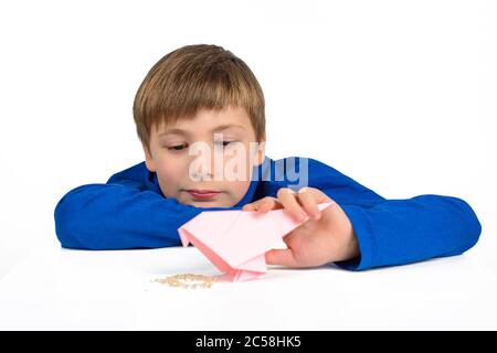 Origami: Ein Schuljunge im blauen T-Shirt sitzt am Tisch und spielt mit einem Papiervogel, will sie füttern Stockfoto