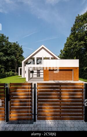 Entworfenes weißes Haus mit großem Garten, Holzhöhe auf Garage und Holzzaun Stockfoto
