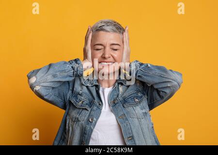 Verärgerte Frau Mittleren Alters, Die Ohren In Stress Bedeckt, Über Gelbem Hintergrund Stehend Stockfoto