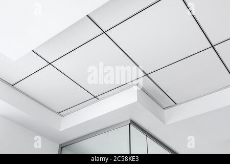 Mehrstufige Decke mit dreidimensionalen Aussprüngen und einer abgehängten Fliesendecke in weißer Farbe, Nahaufnahme geometrischer Details. Stockfoto