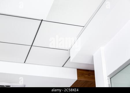 Mehrstufige Decke mit dreidimensionalen Übersprüngen und einer abgehängten Fliesendecke in weißer Farbe, Nahaufnahme geometrische leere Details. Stockfoto