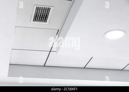 Mehrstufige Decke mit dreidimensionalen Vorsprüngen und einer abgehängten Fliesendecke mit eingebautem runden LED-Licht und Kühlergrill-Lüftungssystem, cl Stockfoto