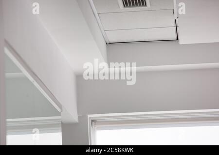 Mehrstufige Decke mit dreidimensionalen Überzügen und abgehängter Fliesendecke mit Rollläden am Fenster. Stockfoto